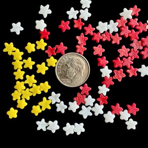 May include: A close-up of a variety of colorful sprinkles in the shape of stars. The sprinkles are red, white, and yellow. A US dime coin is in the center of the image.