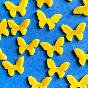 May include: A collection of yellow butterfly-shaped decorations scattered on a blue surface. The butterflies have a textured appearance and are evenly distributed across the frame. The image is a close-up shot.