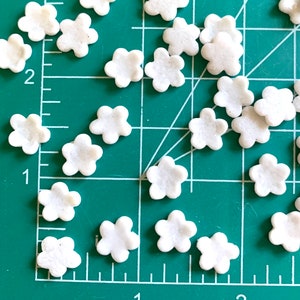 以下が含まれることがあります： 緑色のカッティングマットの上に、白い五芒星型のシュガー スプリンクルが置かれています