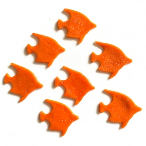 May include: Seven orange fish-shaped cookie cutters on a white background.