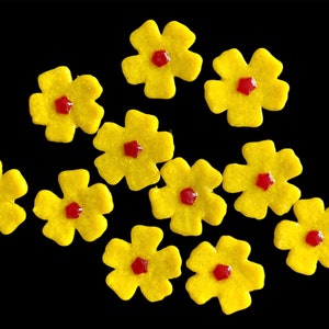 May include: Ten yellow flower-shaped cookies with red centers. The cookies are arranged on a black background.