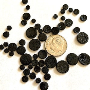 May include: A collection of black, round, textured, ceramic tiles of various sizes. The tiles are scattered on a white surface with a US dime for scale.