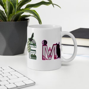 Könnte beinhalten: Weiße Keramiktasse mit dem Wort "IME" in farbenfrohen, stilisierten Buchstaben. Das "I" zeigt einen Mond und ein Gebäude, das "M" hat ein Gebäude und ein Unendlichkeitssymbol, und das "E" hat ein Bienen- und Wabenmuster. Rechts ist eine schwarze Eule.