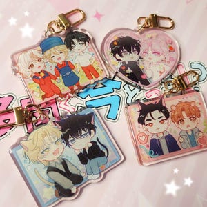 May include: Four acrylic keychains featuring anime-style character illustrations. One is heart-shaped, while three are rectangular. Each keychain includes a gold-toned metal lobster clasp and displays pairs of characters with colorful outfits and cat ears.