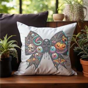 May include: A white pillow featuring a black and colourful bow design. The bow is decorated with a skull, eyeballs, a snake, a spider, a pumpkin, and a moth.