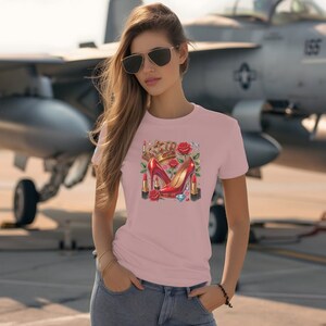 Puede incluir: Una camiseta rosa con un dise&ntilde;o gr&aacute;fico de tacones altos rojos, una corona, pintalabios y una rosa. El dise&ntilde;o est&aacute; centrado en la camiseta.