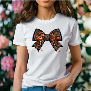 May include: White t-shirt featuring a black bow decorated with Halloween-themed embellishments, such as pumpkins, spiders, and skulls.