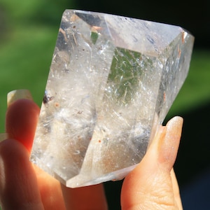 May include: A large, clear quartz crystal with a natural, faceted shape. The crystal has a cloudy, milky appearance with visible inclusions.
