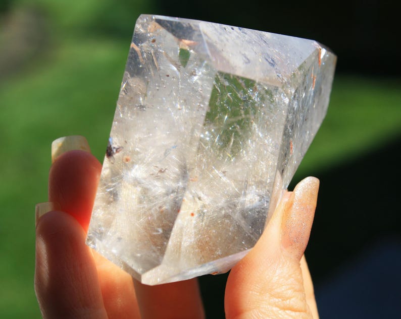 May include: A large, clear quartz crystal with a natural, faceted shape. The crystal has a cloudy, milky appearance with visible inclusions.
