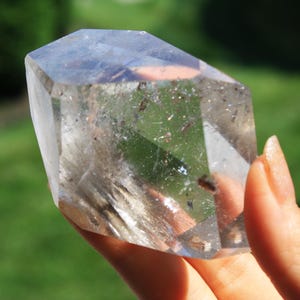 May include: A clear quartz crystal with a faceted, geometric shape. The crystal has a slightly cloudy appearance with inclusions of other minerals.