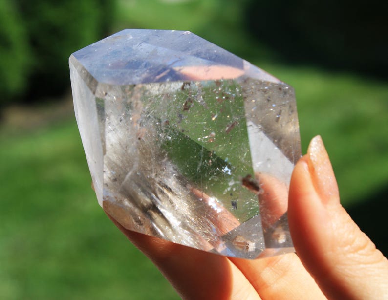 May include: A clear quartz crystal with a faceted, geometric shape. The crystal has a slightly cloudy appearance with inclusions of other minerals.