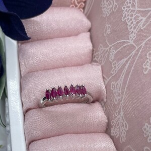 Peut inclure: Une bague avec une rangée de pierres précieuses rouges serties d'argent. La bague est présentée dans un écrin à bague en velours rose.