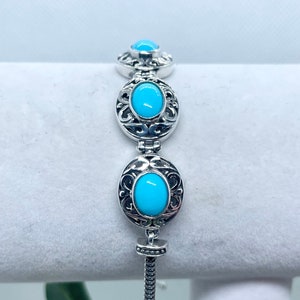 Puede incluir: Un brazalete de plata con tres piedras turquesa engastadas en marcos de plata ornamentados. El brazalete tiene un cierre deslizante.