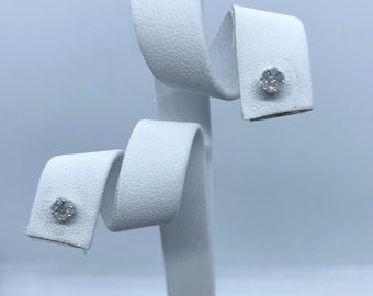 May include: A pair of small diamond earrings on a white display stand. The earrings are set in a cluster of small diamonds.
