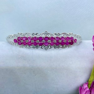 May include: A silver bracelet with a delicate filigree design and a row of pink oval-shaped gemstones.