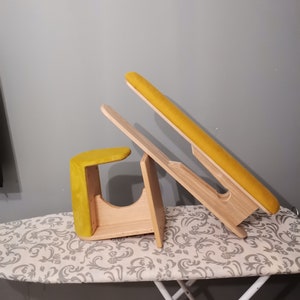 May include: A wooden ironing board with a yellow padded surface. The board is folded and resting on a white ironing board.