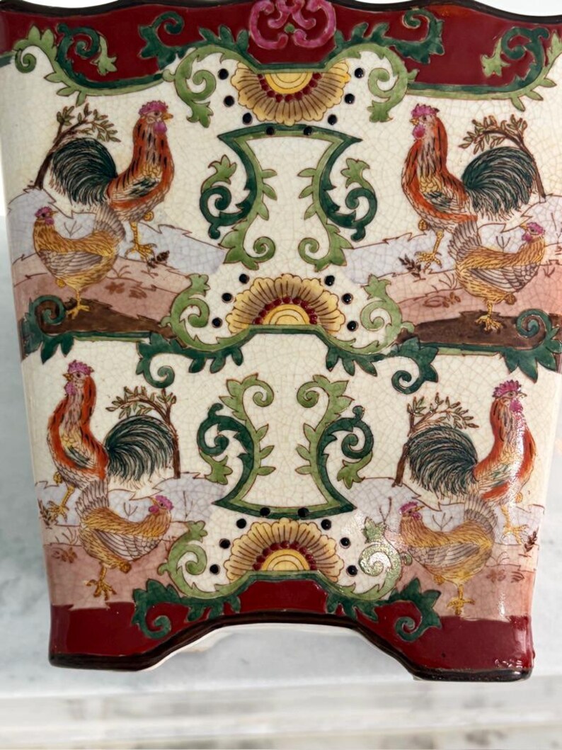 May include: A ceramic vase with a cream-coloured crackle glaze finish, featuring a repeating pattern of roosters and hens in shades of red, orange, and green. The design includes ornate scrollwork and a deep red border at the top and bottom.