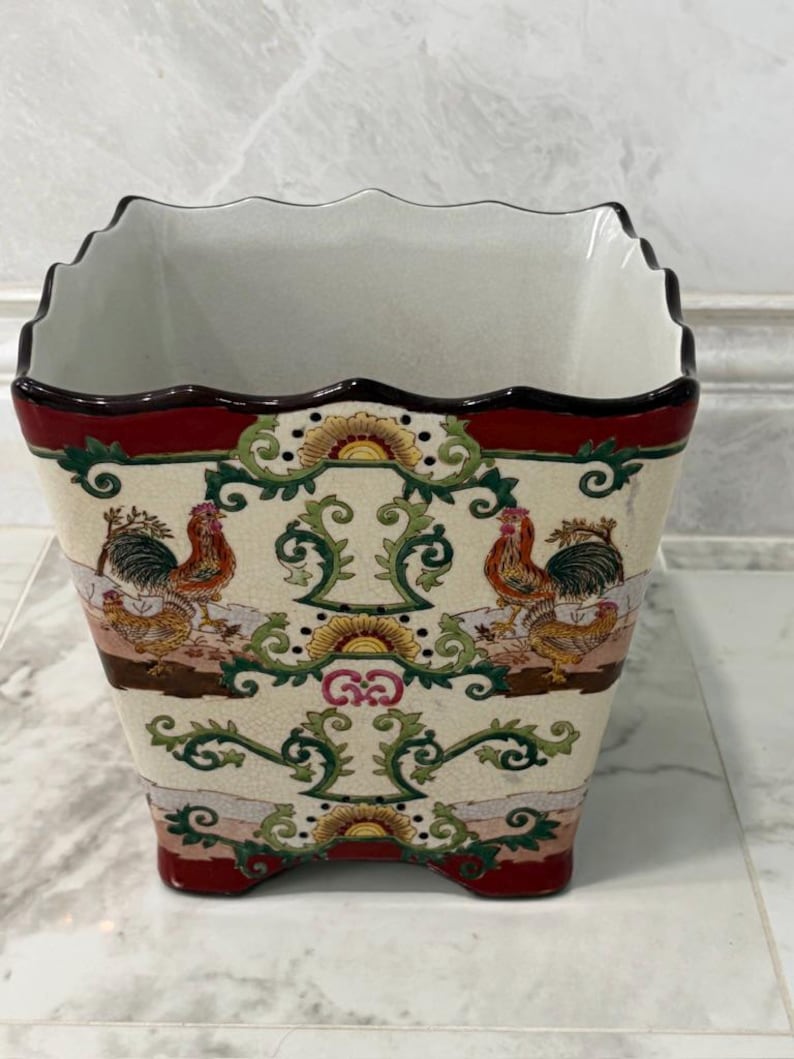 May include: A square ceramic planter with a scalloped rim and a cream-coloured crackle glaze finish. The exterior features a repeating pattern of roosters, green scrolling vines, and yellow sunburst motifs, framed by deep red bands at the top and base.