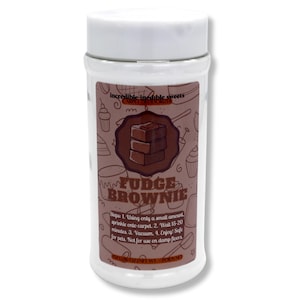 May include: A clear plastic jar with a white lid, labeled "Fudge Brownie." The label features a brown graphic of a brownie and instructions for use. The jar contains a white powder and is designed to be sprinkled on carpets.