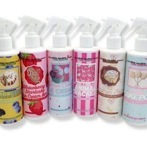 May include: Six white plastic spray bottles labeled Incredible Inedible Sweets Fabric Refresher. Scents include Lemon Berry Pound Cake, Strawberry Shortcake Ice Cream Bar, Cotton Candy Ice Cream, Animal Crackers, Iced Cinnamon Rolls, and Confetti Cake Pop.