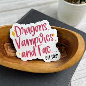 May include: White sticker with pink lettering that reads "Dragons, Vampires, and Fae... Oh my!"