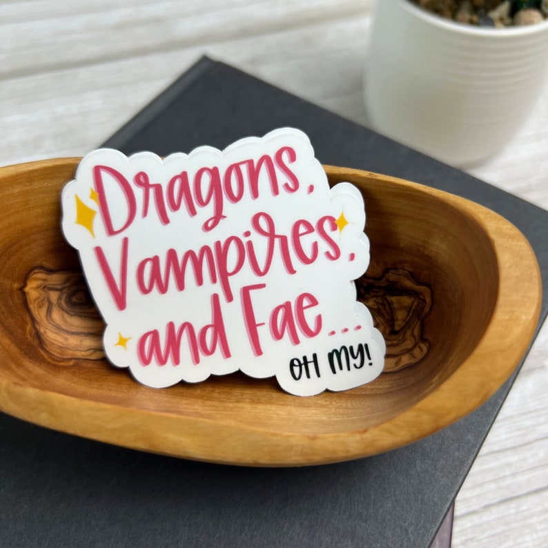 May include: White sticker with pink lettering that reads "Dragons, Vampires, and Fae... Oh my!"