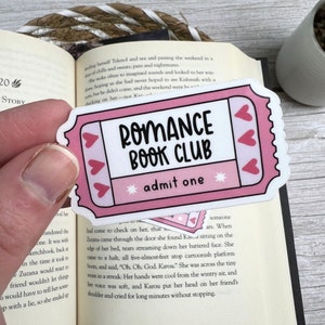 May include: Pink and white ticket-shaped sticker with the text "Romance Book Club" and "admit one" in black lettering. The sticker has a pink and white heart design.