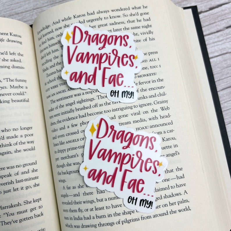 May include: Three colorful stickers with the text "Dragons, Vampires, and Fae... Oh my!" in a whimsical font. The stickers are on a book page with text about angels and mythical creatures.