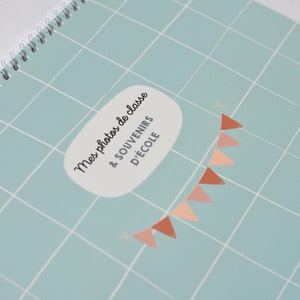 May include: A light blue photo album with a white grid pattern and a white speech bubble with the text "Mes photos de classe & souvenirs d'&eacute;cole" in black. A string of peach and brown triangle flags hangs from the top of the speech bubble.
