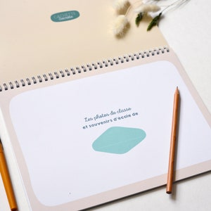 May include: A spiral bound book with a light beige cover and a teal blue graphic. The cover text reads "Les photos de classe et souvenirs d'&eacute;cole de".
