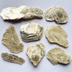 Pode incluir: Uma coleção de oito espécimes minerais de mica verde bruta e natural. A mica é em camadas e translúcida, com um leve brilho.