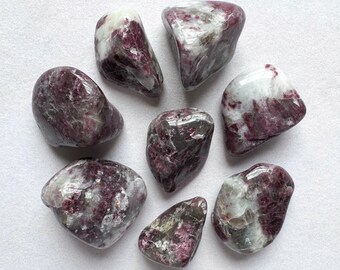 May include: A collection of eight tumbled stones with a mix of white and purple hues. The stones are smooth and polished, with a variety of shapes and sizes.