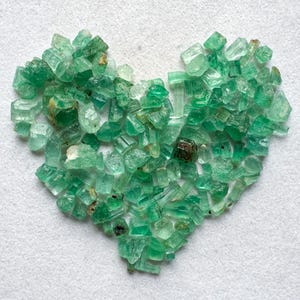 May include: A heart-shaped arrangement of green emerald crystals, showcasing a variety of sizes and shapes.
