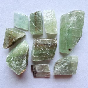 May include: A collection of eight green and white crystal stones with a rough, natural texture. The stones are various sizes and shapes, with some having a darker green hue.
