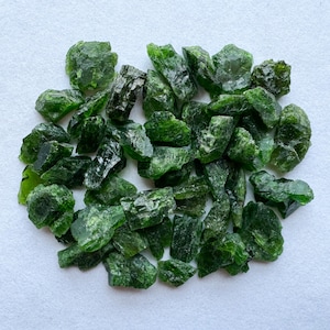 May include: A collection of green, rough, and unpolished gemstone chips. The chips are various sizes and shapes, and have a natural, raw appearance.