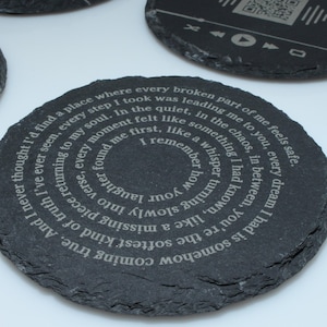 May include: Dark gray slate coasters with engraved text and designs. One coaster features a spiral of text, another has a sound wave pattern, and a third has music control icons. These coasters are a unique home decor item.
