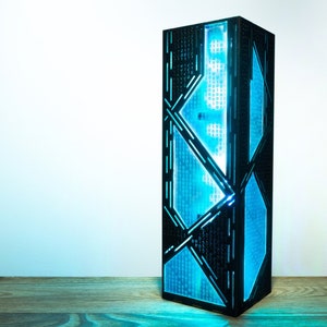 Peut inclure: Une lampe géométrique noire avec une lumière bleue qui brille à travers le motif complexe. La lampe est posée sur une surface en bois.