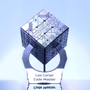 Puede incluir: Un trofeo plateado con una parte superior en forma de cubo con diseños de circuitos grabados y la palabra "SYNCHRONIZATION". La base muestra los nombres "Leo Carter" y "Code Master".