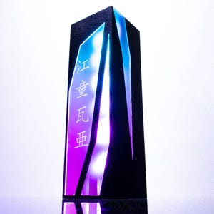 May include: A tall, rectangular black pillar lamp featuring vertical, angular cutouts illuminated with a gradient of blue to purple light. The front panel displays three vertical Chinese characters in white, glowing against the vibrant light.