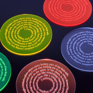 Pode incluir: Tábua de cortar circular em tons de verde, vermelho e azul, cada uma com uma borda brilhante. As tábuas de cortar apresentam um design de texto em espiral com uma citação. As tábuas de cortar são um item decorativo.