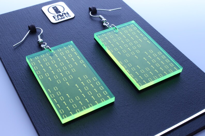 K&ouml;nnte beinhalten: Ein Paar rechteckige, neongr&uuml;ne Ohrringe mit silbernen Haken. Jeder Ohrring hat ein Muster aus wei&szlig;em Bin&auml;rcode. Die Ohrringe werden auf einer dunklen Oberfl&auml;che mit einem kleinen Logo in der oberen linken Ecke pr&auml;sentiert.
