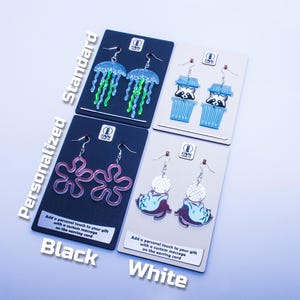 K&ouml;nnte beinhalten: Vier Paar Ohrringe auf Karten pr&auml;sentiert. Die Designs umfassen Quallen, Waschb&auml;ren in Bechern, rosa Blumenformen und ein Wesen mit einem gepunkteten Kreis. Die Karten sind schwarz und wei&szlig;, mit dem Text "Personalized Standard Black White".