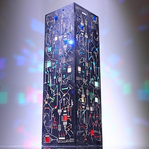 May include: A tall, rectangular black pillar lamp featuring an intricate, glowing circuit board pattern on its surface. The design includes illuminated lines and geometric shapes in vibrant shades of blue, red, and green, creating a tech-inspired aesthetic.