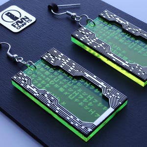 Könnte beinhalten: Ein Paar rechteckige Ohrringe mit neongrünem und transparentem Design. Die Ohrringe haben ein schwarz-weißes Leiterplattenmuster an den Rändern. Die Ohrringe liegen auf einer dunklen Oberfläche mit einem weißen quadratischen Logo "FVN CRAFTS".