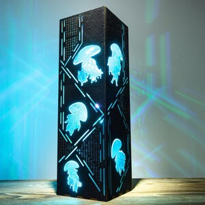 May include: A tall, rectangular black lamp with a textured surface featuring cut-out designs of glowing blue jellyfish. The light shines through the jellyfish shapes and geometric lines, casting a bright blue and green light onto the surrounding area.