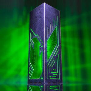 May include: A tall, rectangular, dark-coloured tower structure featuring intricate, laser-cut geometric patterns on its sides. The cutouts reveal a bright, glowing green light emanating from within, highlighting the detailed circuit-like design.