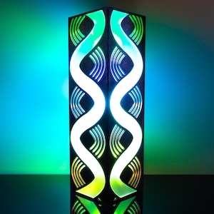 May include: A rectangular, illuminated lamp with a black frame and a vibrant, colorful design. The lamp features a central, white, double-helix pattern, with green, blue, and yellow accents. The lamp is on a reflective surface.
