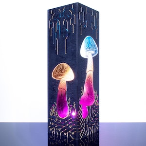 May include: A tall, rectangular black lamp featuring laser-cut mushroom designs that glow with vibrant blue, pink, and orange light. The surface is etched with intricate circuit board patterns that extend from the base to the top of the structure.