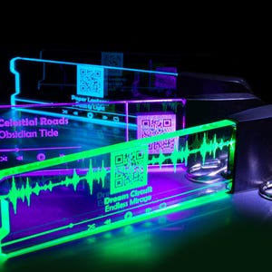 Könnte beinhalten: Drei beleuchtete Acryl-Schlüsselanhänger mit schwarzem Sockel und silbernen Schlüsselringen. Die Schlüsselanhänger zeigen Songtitel und QR-Codes mit leuchtenden Neonfarben in Grün, Blau und Lila. Der Text auf den Schlüsselanhängern lautet "Celestial Roads Obsidian Tide", "Dream Circuit Endless Mirage" und "Paper Lanterns Family Light".