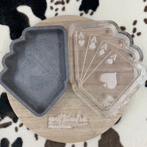 Puede incluir: Un juego de cuatro bandejas de acrílico transparente con forma de cartas de juego, cada una con un palo de as diferente. Las bandejas están apiladas una encima de la otra y están sobre una superficie de madera. Las bandejas están diseñadas para ser utilizadas como bandeja de servir o como pieza decorativa.